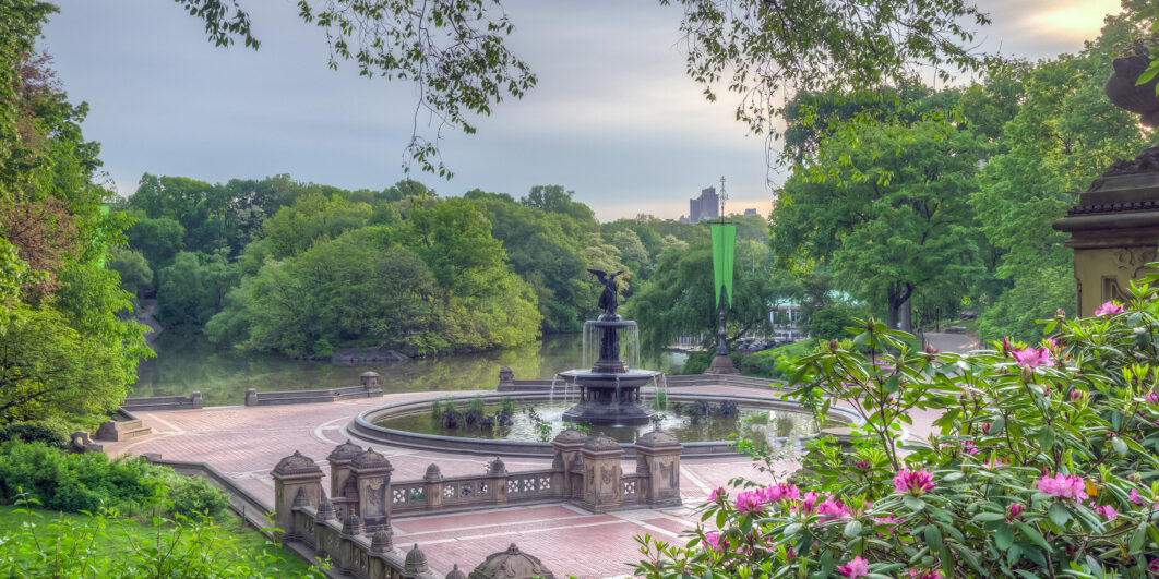 Scenic view of a historic fountain surrounded by greenery and flowers in a park.