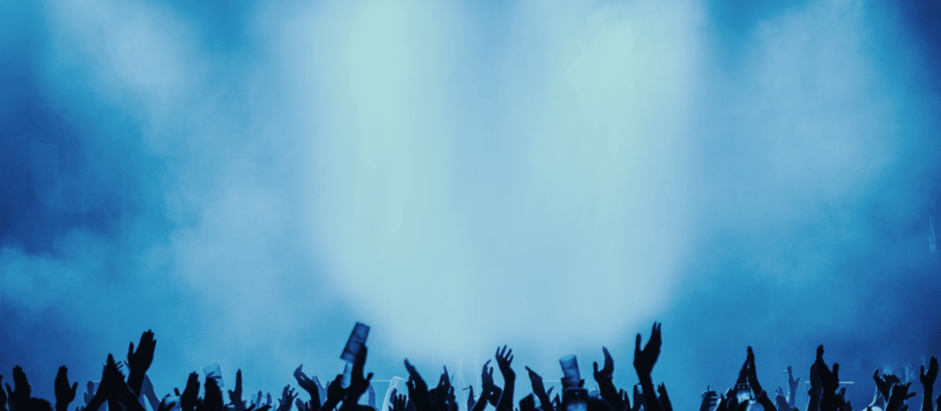 Concert crowd raising hands under dramatic blue lighting.