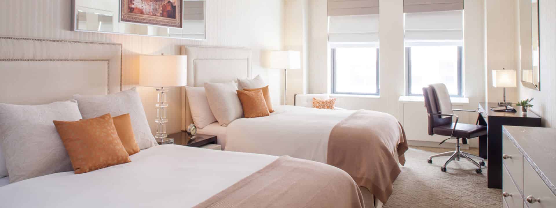 Elegant hotel room with two beds, a desk, and soft lighting.