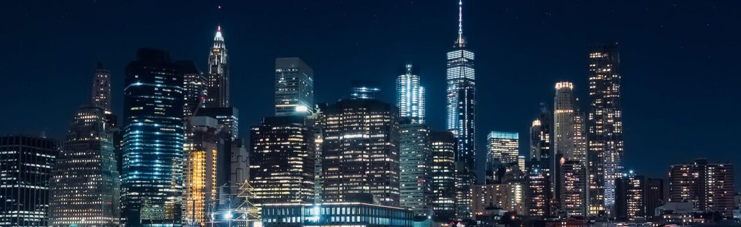 New York City skyline at night with illuminated skyscrapers.