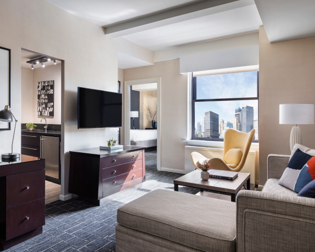 Modern hotel living room with large windows and city views.