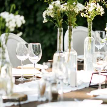 Outdoor dining table with white flowers and glassware.