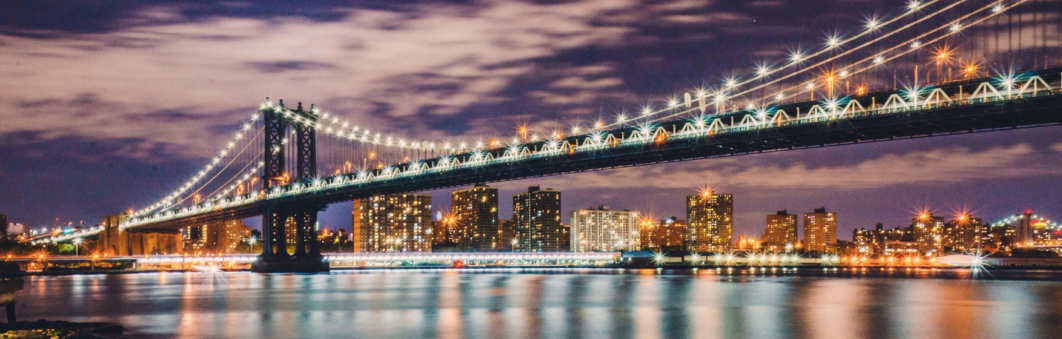 Manhattan Bridge illuminated at night over water.