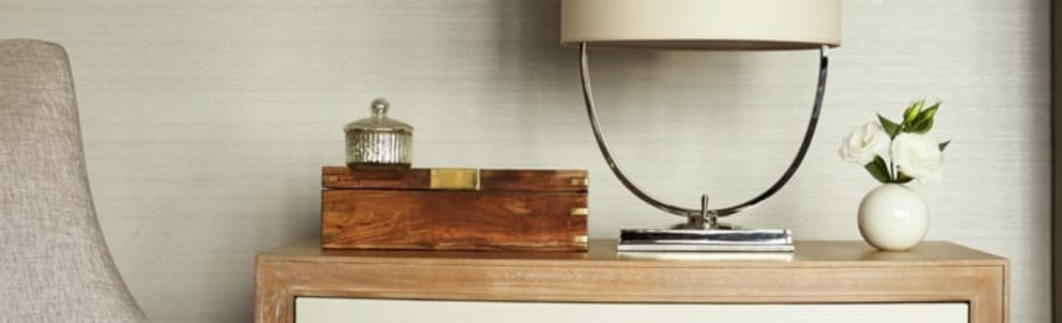 Wooden nightstand with a lamp, wooden box, and small vase with white flowers.