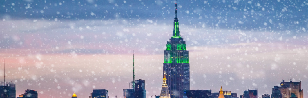 Empire State Building glowing green with snowfall in the foreground.