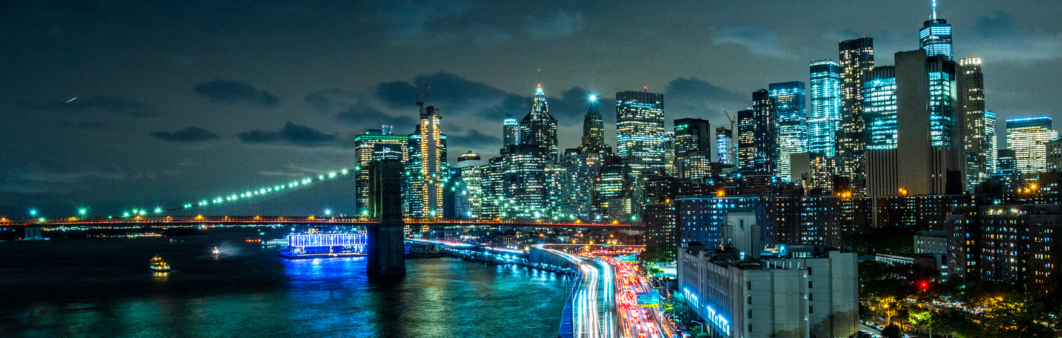 Night skyline of New York City with illuminated skyscrapers and bridges.