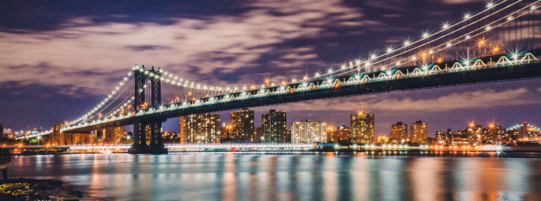 Illuminated suspension bridge at night with city skyline.