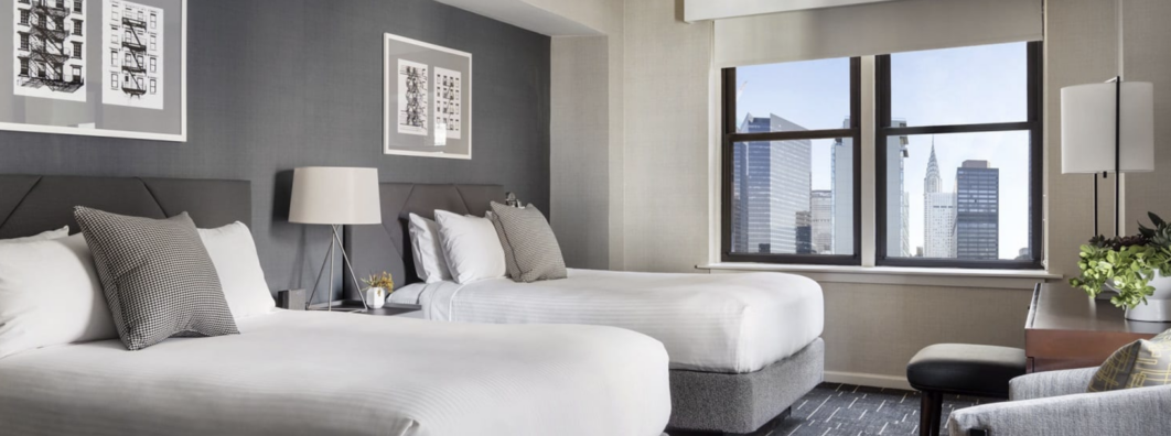 Modern hotel room with a king-size bed, stylish decor, and city view.